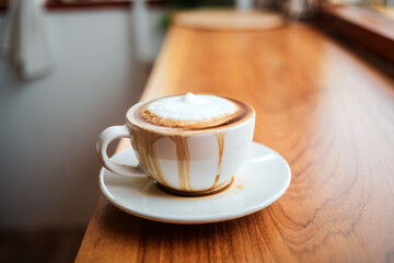 Spilled coffee with milk in a white cup or cappuccino is overflowing from the coffee cup on wooden...