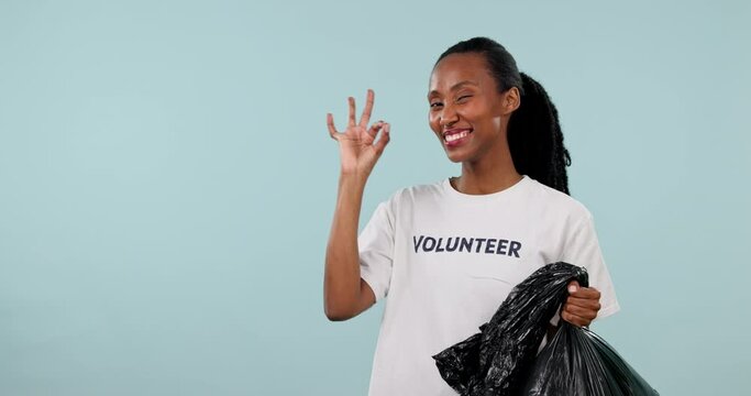 Plastic bag, black woman point or volunteer okay wink for trash cleaning news, climate change and charity recycling. Studio mockup space, ok emoji icon or Nonprofit portrait person on blue background