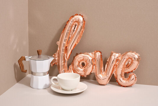 Foil balloon in the form of the word love and geyser coffee maker, white cup hot coffee.