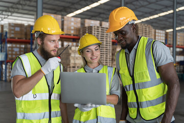 Group of male and female warehouse worker in safety vest and helmet working with laptop computer in industry storage warehouse