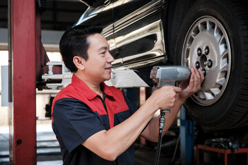 One expert Asian male automotive mechanic technician is screwing car wheel nuts on lifting with...
