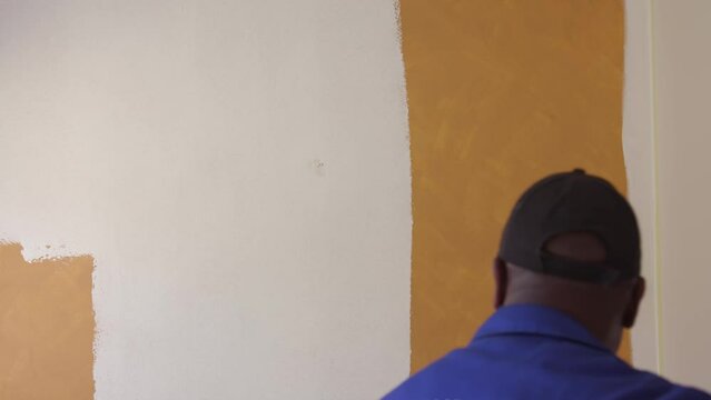 South Africa black man using a roller to paint interior wall in house white removing old paint colour priming wall