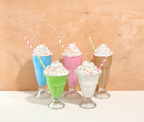 Appetizing sweet colorful milkshakes with soft white cream and colored sprinkles in glasses on a wooden background. Festive and colorful mood.