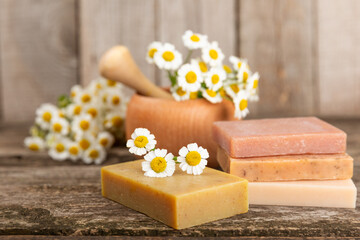 Obraz na płótnie Canvas Natural homemade soap with chamomile flowers on a wooden table. Close-up of moisturizing soap with natural herbal oils. Spa and beauty concept. Place for text. Copy space.Fletley