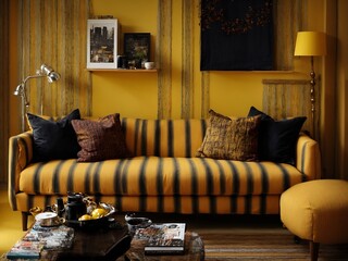 A living room with a black and yellow striped sofa, a bright yellow lamp and various textiles in complementary shades.