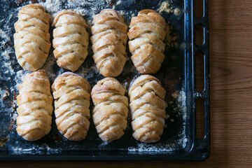 Traditional russian pies pirozhki on baking pan on brown table, top view, selective focus.