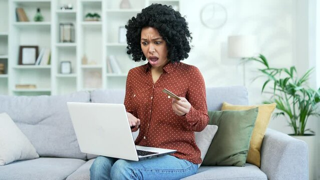Frustrated young african american female discovered fraud while entering credit card number on laptop sitting in living room at home. Sad black woman saw that money had been stolen from her account