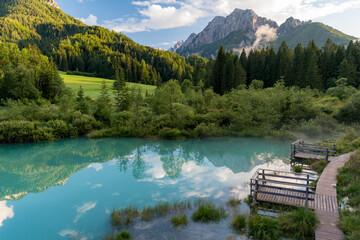 Reflection of mountains and clouds in a turquoise lake surrounded by pine trees in the alps of Slovenia