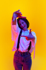 Cheerful woman in stylish white shirt with suspenders posing against orange studio background in neon light. Concept of human emotions, fashion, lifestyle, facial expression, ad