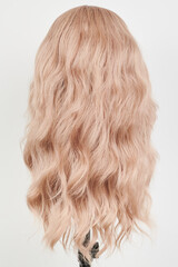 Naklejka premium Natural looking blonde wig on white mannequin head. Long hair on the plastic wig holder isolated on white background, back view.