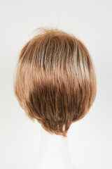 Natural looking blonde fair wig on white mannequin head. Short hair cut on the plastic wig holder isolated on white background, back view.