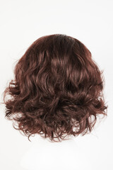 Naklejka premium Natural looking dark brunet wig on white mannequin head. Middle length brown hair on the plastic wig holder isolated on white background, back view.