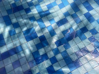  Close up of shallow swimming pool bottom, water flowing into the pool with blue color ceramic texture background.