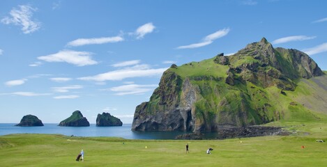 Green golf course next to the elephant rock in Westman Islands, Iceland