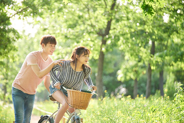 A young male and female couple are enjoying a walk on a bicycle in the park. - obrazy, fototapety, plakaty