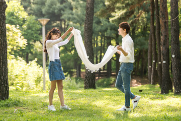 A young couple using a large towel to have fun in a forested park