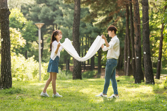 A young couple using a large towel to have fun in a forested park