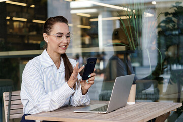 The financier works online using a computer.  A woman with glasses and a modern laptop in office clothes, a bank employee. A business woman uses a phone, writes a message to a client.