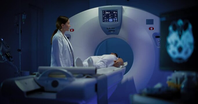 In Medical Laboratory Radiologist Controls MRI or CT or PET Scan with Female Patient Undergoing Procedure. High-Tech Modern Medical Equipment. Friendly Doctor Chats with Patient