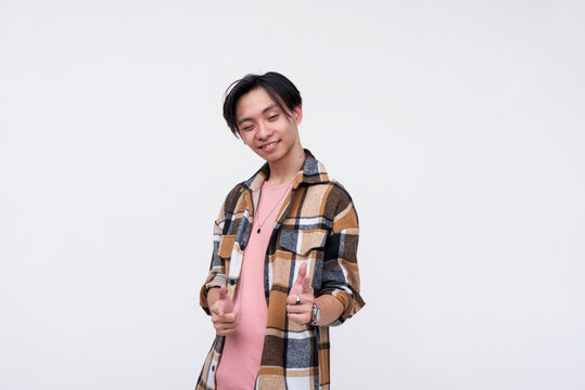 A smug and confident young asian man makes a finger gun gesture while winking. Isolated on a white background.