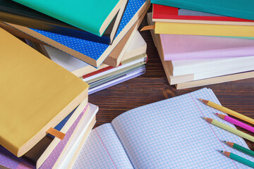 Stacks of different books, open notebook and pencils on rustic table. Copy space