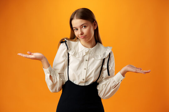 Teen girl shows I don't know gesture against yellow background