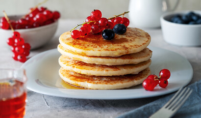 Pile of pancakes with red currants, blueberries and honey on a grey plate with fork