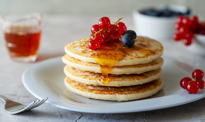 Pile of pancakes with red currants, blueberries and honey on a grey plate with fork