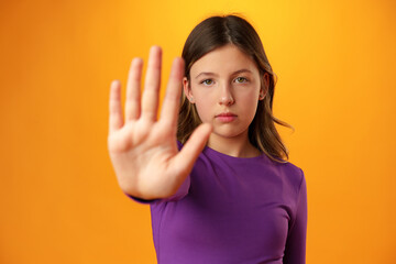 Teen girl extend hand in block gesture against yellow background - obrazy, fototapety, plakaty