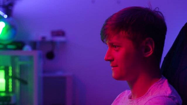 Close-up side view of cheerful young male gamer playing online computer video game in dark room at home. Closeup emotions on face of young man playing computer games. Shooting in slow motion.