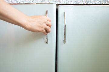 Woman's hand opens kitchen cabinet under sunlight, kitchen furniture