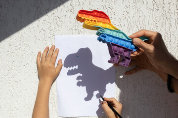 child traces a contrasting shadow from a dinosaur on paper on a sunny day. happy cheerful...