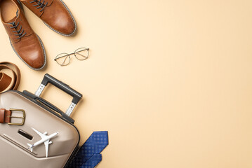 International work expedition theme. Top view of miniature plane, formal outfit details – belt, sophisticated tie, leather shoes, suitcase on pastel beige backdrop with space for text or advert