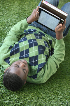 A Boy In An Argyle Sweater Lays On The Grass Reading From An Electronic Notebook; Portland, Oregon, United States of America