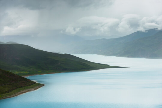 Hilly and mountainous landscape with sacred lake under a cloudy sky; Shannan xizang china