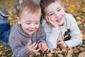 Portrait of two young boys laying on fallen leaves in autumn colours; St. albert alberta canada