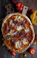 Pumpkin pizza with salami, red onions and mozzarella cheese on wooden table