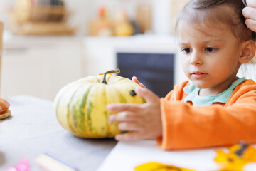 Fototapeta premium Toddler girl having fun at home. Happy Family preparing for Halloween. Portrait of cute kid making Halloween home decorations while sitting at table.