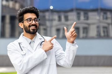 A young Hindu doctor from outside the clinic smiles and looks away, the man points his fingers in the direction, smiles with satisfaction and the doctor with a medical coat and a stethoscope.