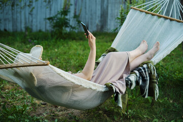 Embracing Slow Living: Woman Finds Solitude in Backyard Hammock, Smartphone in Hand for a Mindful...