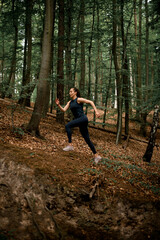 Naklejka na ściany i meble Full length photo of fitness female athlete running uphill on forest path in summer day