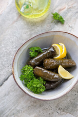Bowl with greek dolmades, fresh parsley and lemon wedges on a light-grey granite background, elevated view, vertical shot