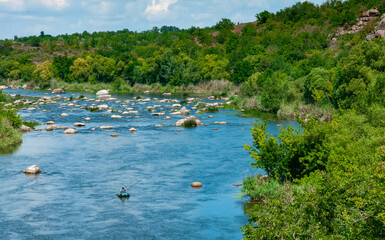 A fisherman in a rubber boat catches fish behind rock rifts in the middle
