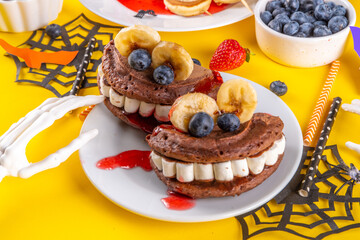 Funny kids breakfast for Halloween. Creative homemade sweet pancakes in form of traditional Halloween monsters and symbols, with fresh berry, chocolate and red syrup
