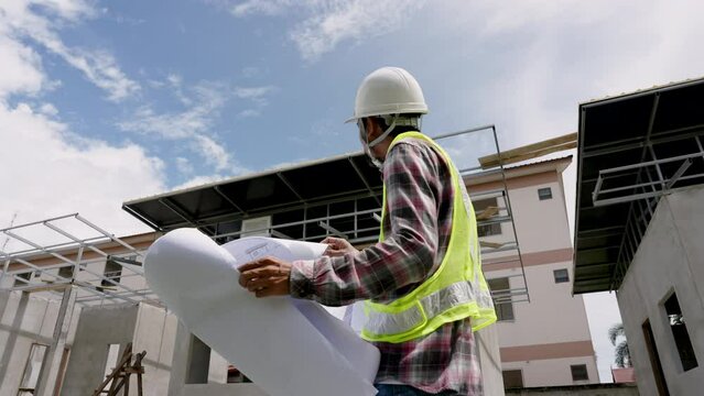 Mustache Asian man wearing a green reflective vest and safety helmet. Standing outside a house under construction Mustache of an Indian architect Construction plans are being reviewed from blueprints.