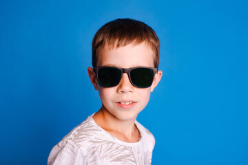 headshot child boy in sunglasses looking at camera isolated over light blue studio background