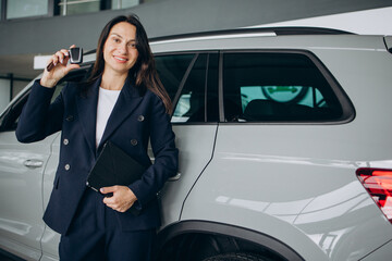 Sales woman in car showroom holding car keys and standing by the car