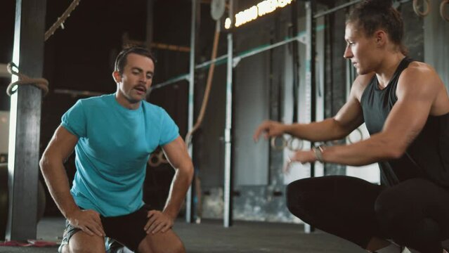 Active man using dumbbells for plank and renegade rows while training in a gym with a personal female trainer, success, and high five.