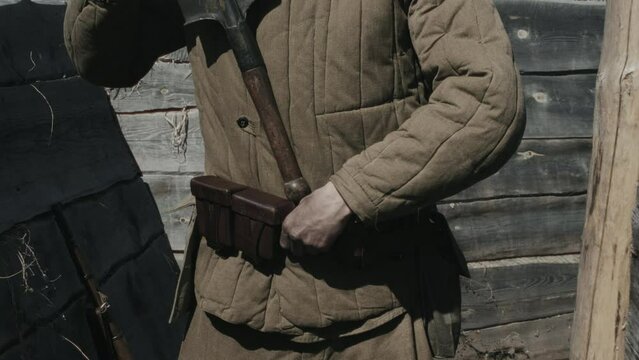 Medium section shot of unrecognizable soldier standing in trench preparing for battle putting small military shovel behind his belt
