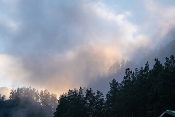 Mountains and peaks in fog at sunrise or sunset. Sun from behind the mountain. Amazing view of mountains and forest landscape with cloudy skies Altai mountains. Mountains and peaks in fog at sunrise